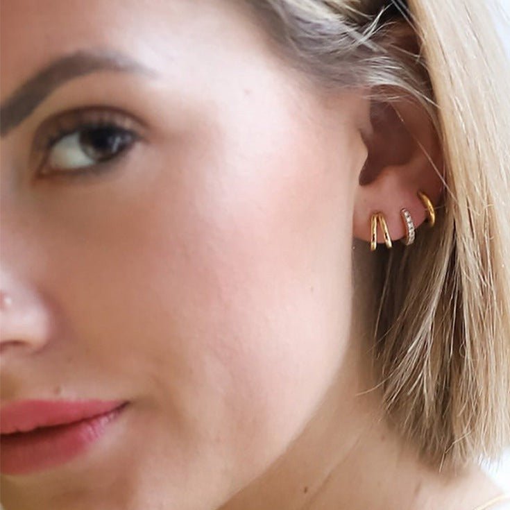 Blonde model's ear adorned with gold Row Huggies Earrings with turquoise stones.