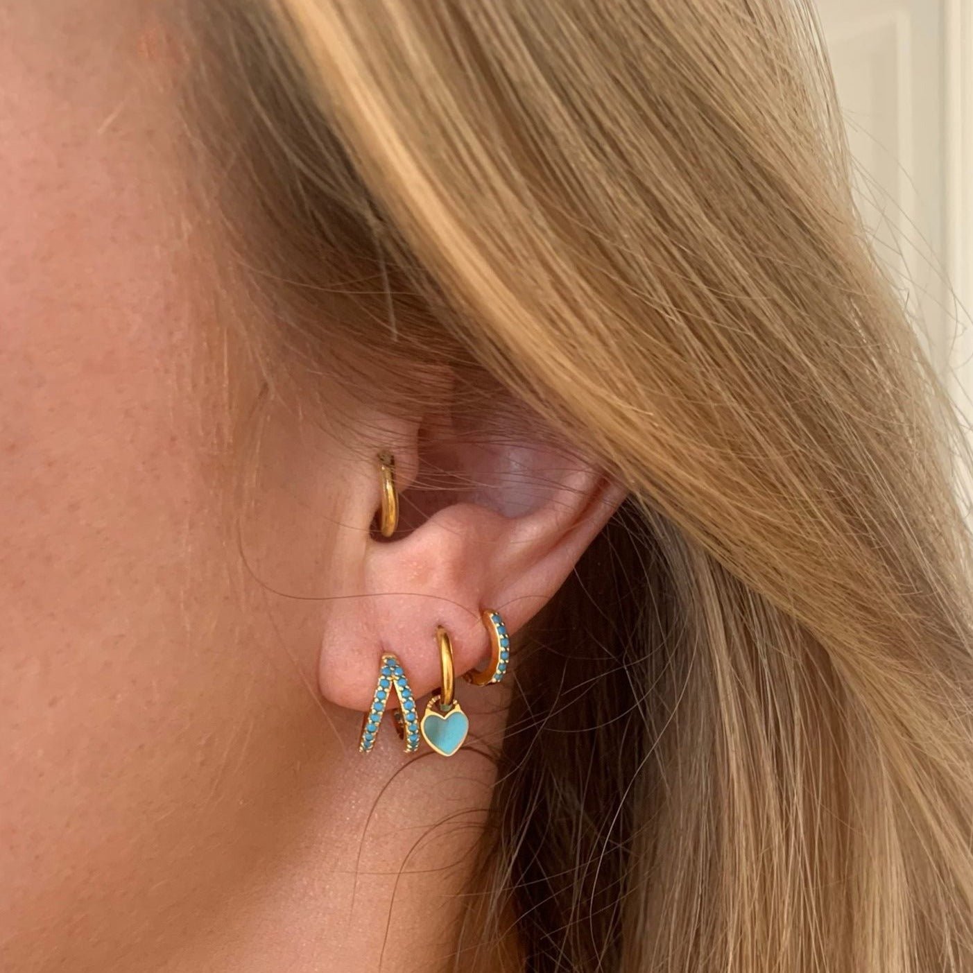 Blonde model's ear adorned with gold Row Huggies Earrings with turquoise stones - IceGlint